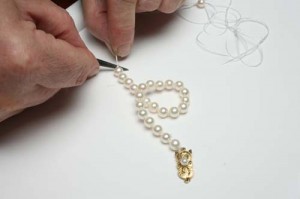 Close up of a jeweler restringing a strand of pearls